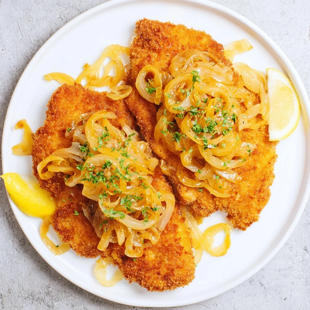 A close-up of a tender Schnitzel with caramelized onions, ready to be enjoyed with lemon wedges.