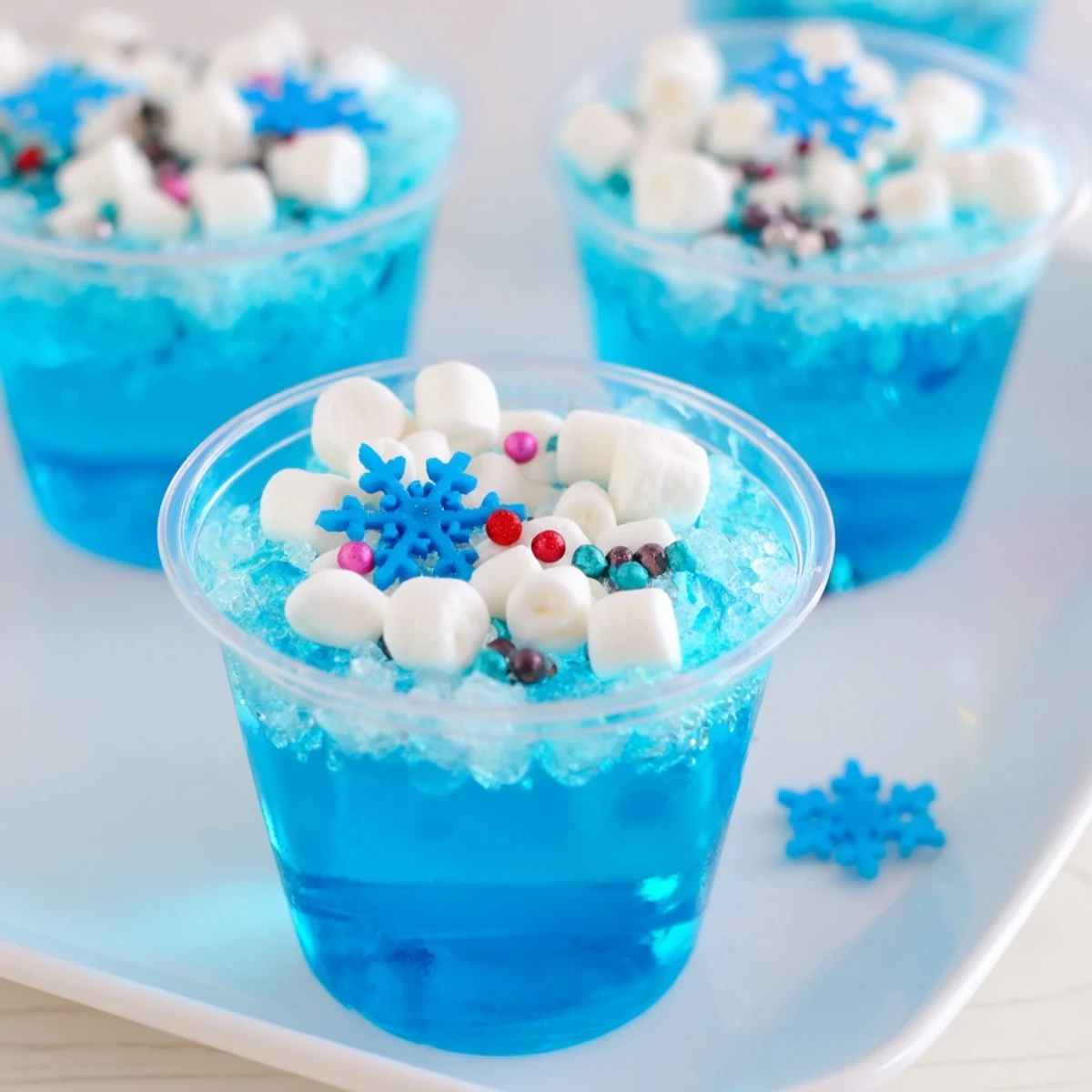 Kühle Snow Globe Jello Cups versprechen Spaß: Blaue Gelee-Schichten, dekoriert mit süßen Schneeflocken und Marshmallows.