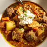 Savory Yemeni Saltah glistening atop bread, topped with airy fenugreek, a classic comfort food.