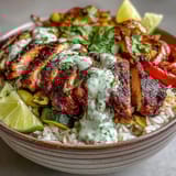 Teller mit würzigem Blackened Chicken, duftendem Reis, lebhaften Paprikastreifen und einem cremigen Limetten-Dip garniert.