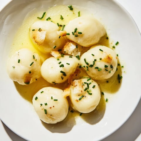 Golden, fluffy potato dumplings drizzled with luxurious truffle oil and fresh chives, a flavorful side.