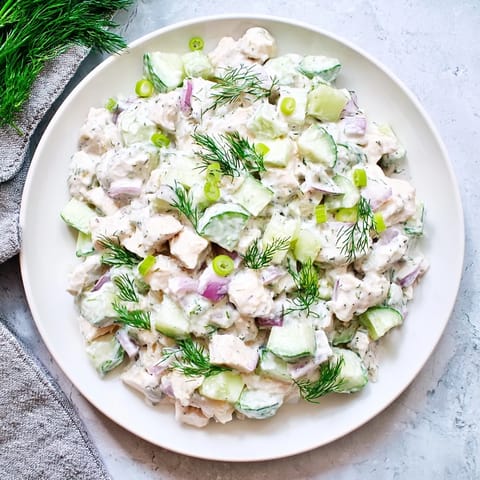 Cremige Gurken Hühnchensalat auf einem hellen Teller, mit knusprigen Gurkenscheiben und frischem Dill garniert.