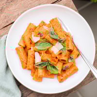 Gekochtes Spicy Rigatoni Pasta in einer cremigen, scharfen Tomatensauce, garniert mit frischem Basilikum und geriebenem Parmesan für US-Foodie-Fotos.  